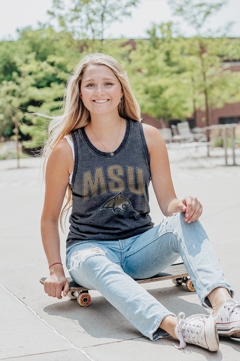 Female model sitting on skateboard wearing a blue 84 college graphic tank top